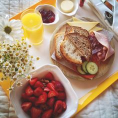 a tray with sandwiches, strawberries and orange juice on it next to some flowers