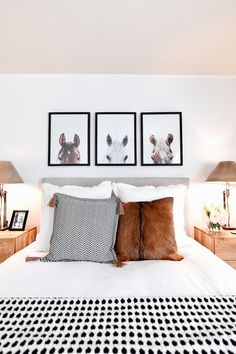 a bed with two pictures on the wall above it and some pillows in front of them