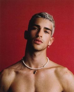 a shirtless man wearing a pearl necklace and pearls around his neck, against a red background