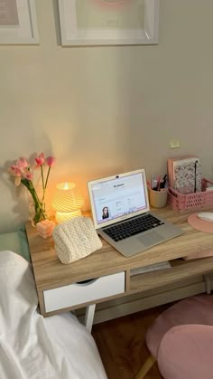 a laptop computer sitting on top of a wooden desk next to a pink chair and lamp