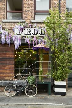 a bicycle parked in front of a building with purple flowers hanging from it's roof