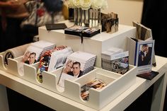 a white table topped with lots of pictures and boxes filled with books next to flowers