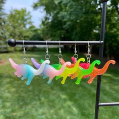 three different colored earrings hanging from a metal rack in front of some grass and trees