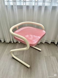 a pink chair sitting on top of a hard wood floor next to a white curtain