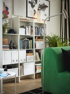 a green couch sitting in front of a white book shelf filled with books and plants