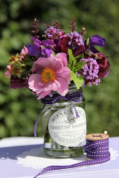 a jar filled with flowers sitting on top of a table next to a purple ribbon