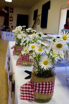 several mason jars with daisies in them are lined up on a long white table