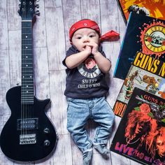 a young boy laying on the floor next to a guitar and some books with his hands in his mouth