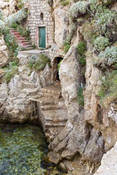 stairs lead down to the water below an old stone building with a green door and window