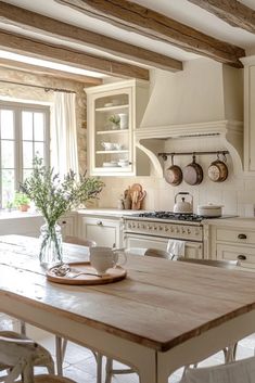 a kitchen with white cabinets and wooden table in the center, surrounded by hanging pots and pans