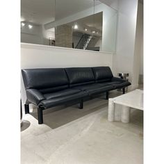 a black leather couch sitting next to a white table in a room with mirrors on the wall