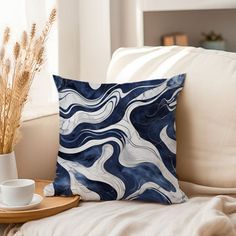 a blue and white pillow sitting on top of a couch next to a cup filled with coffee