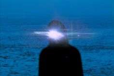 a man standing in front of the ocean with his head turned to the side and light shining from behind him