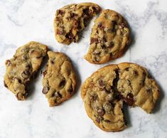 four chocolate chip cookies on a marble counter top with one broken in half and the other partially eaten