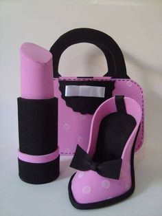 a pink and black purse, lipstick holder, and pair of slippers are on a white surface