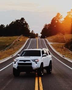 a white suv driving down the road at sunset