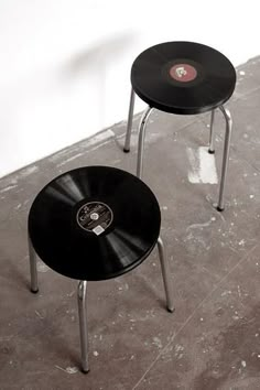 two small black tables sitting next to each other on top of a cement floor in front of a white wall