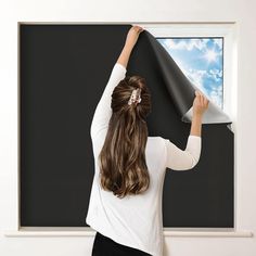 a woman is holding up a black wallpaper in front of a window with blue sky and clouds on it