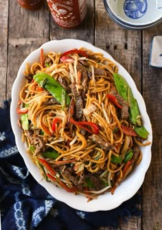 a white bowl filled with noodles and meat on top of a wooden table next to sauce