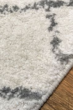 a white rug with black and grey designs on the top, sitting on a wooden floor