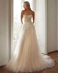 a woman standing in front of a window wearing a wedding dress