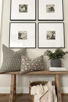 four framed pictures hang on the wall above a wooden bench with a basket and blanket