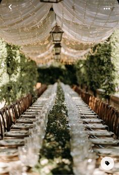 the long table is set with clear glassware and place settings for guests to sit at