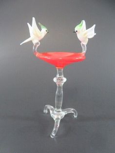 two glass birds sitting on top of a red bowl in front of a black background