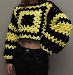 a woman wearing a black and yellow crochet cropped sweater standing in front of a wall