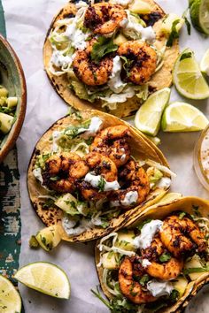 three shrimp tacos with lime wedges and cilantro sauce on the side