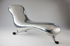 a shiny silver chair sitting on top of a white floor next to a gray wall