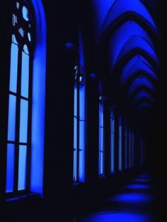 an empty hallway with blue light coming through the windows and dark lighting on the walls