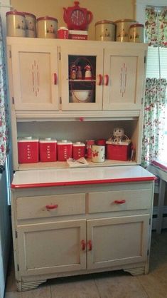 an old fashioned kitchen with red and white pots on the top shelf, cabinets below