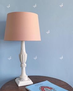 a lamp on a table next to a book and a blue wall with white birds