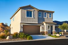 a two story house in the middle of a desert area with rocks and bushes around it