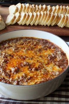 a white bowl filled with cheese and bread on top of a wooden table next to sliced bread