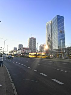 two yellow trains are on the tracks in front of some tall buildings and people walking down the street