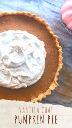 a pumpkin pie with whipped cream in a pie pan on a blue table cloth next to an orange and pink pumpkin