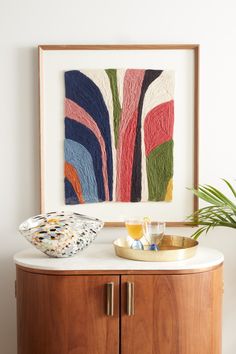 an art work is displayed on the wall next to a bowl and tray with drinks