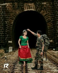 a woman in a red and green dress standing next to a soldier on train tracks