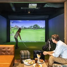 a man and woman playing golf on a large screen in a living room with couches