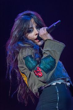 a woman with long hair holding a microphone up to her ear and wearing a jacket