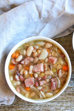 two bowls of soup with ham, beans and carrots next to a napkin on a wooden table