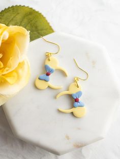 For all the Snow White lovers!  Drop Length: 1.6 in. (Ears are 1.25 in. height)  Colors: Soft Yellow with Blue and Red Earring Hardware: 18k Gold-Plated Hooks Care instructions Please note that Wild Honey Clay earrings are handcrafted with polymer clay and must be handled with delicate care. Do not bend the earrings.  Store them in their box when traveling to ensure protection & do not keep them in direct sunlight. Return Policy We do not accept returns or exchanges on our earrings. However, if one breaks due to a flaw in the design, we will send a replacement if it's within two weeks of your purchase date. In Ears, Wild Honey, Ear Earrings, Soft Yellow, Red Earrings, Disney Inspired, Beauty And The Beast, Clay Earrings, Jewelry Earrings Dangle