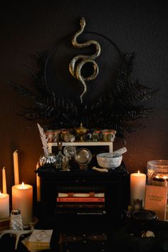 candles are lit in front of a table with books and other items on it, along with a snake sculpture