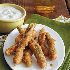 some fried food on a white plate next to a bowl of yogurt and dip