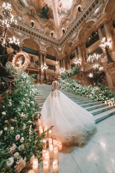 a woman in a wedding dress is standing on the stairs with flowers and candles around her