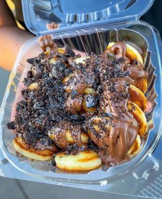 a plastic container filled with lots of chocolate covered donuts and toppings on top