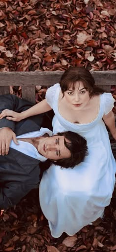 a man and woman are laying on the ground in front of some leaves, looking up at the camera