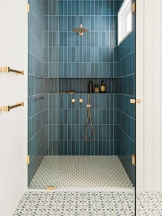 a blue tiled shower with gold handles and brass fixtures in a bathroom area that has white walls and tile flooring